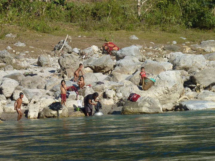 Mom washes the clothes, the kids play in the river